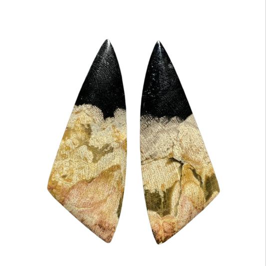 Pair of unique earrings with black and beige design held between fingers against a dark background